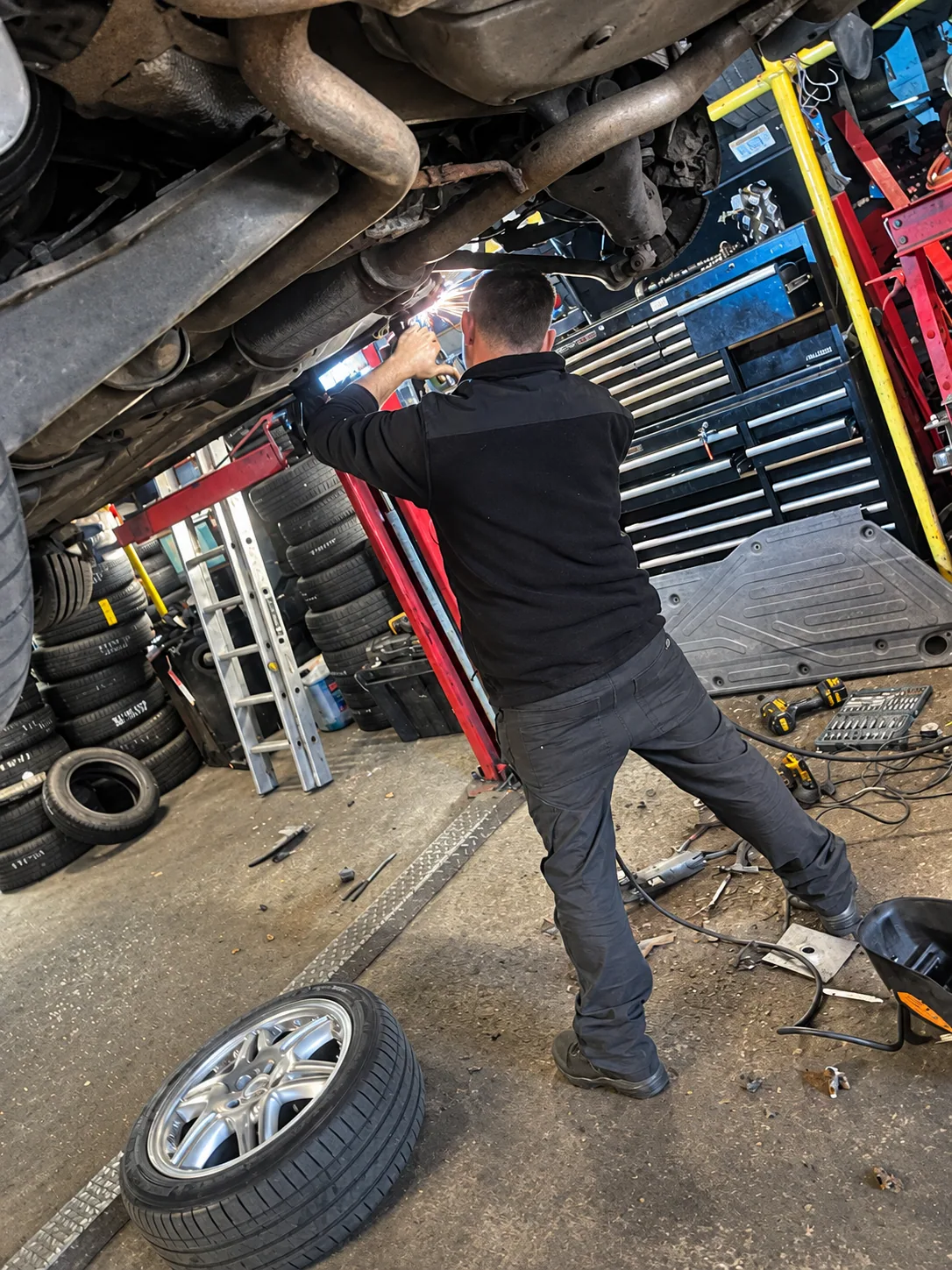 Mechanic welding an exhaust beneath a raised vehicle at Norwich Garage